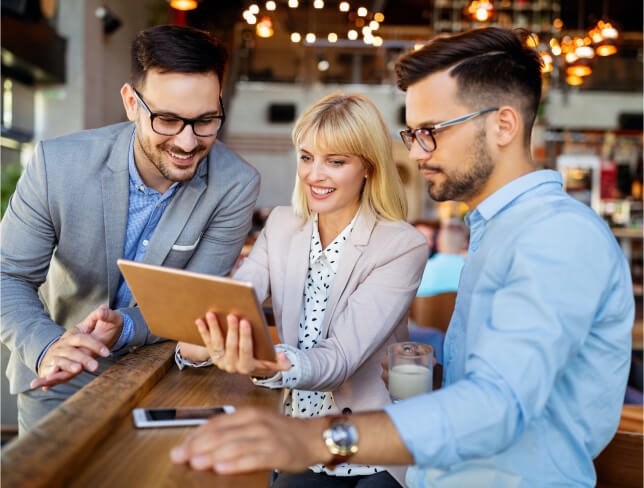 Three professionals collaborating around a tablet in a bright modern workspace